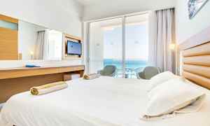 Hotellihuone, jossa sänky, kirjoituspöytä ja parveke merinäköalalla. (Tekoälyn luoma teksti)