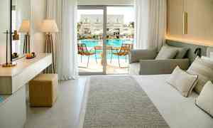 Hotellihuone, jossa on sänky, sohva ja parvekkeen ovi näkymällä uima-allasalueelle. (Tekoälyn luoma teksti)