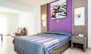 Hotellihuone, jossa on parivuode, sängyn takana violetti seinä ja yöpöytä. (Tekoälyn luoma teksti)