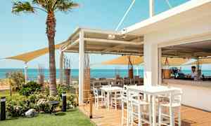 Ulkoterassiravintola, jossa pöytiä ja tuoleja, merinäköala ja kirkas sininen taivas. (Tekoälyn luoma teksti)