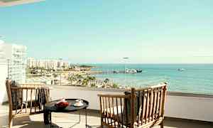 Kaksi puutuolia ja pöytä hotellin parvekkeella, josta on näkymä rannalle ja merelle. (Tekoälyn luoma teksti)