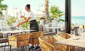 Ulkoterassi meren rannalla, taustalla palmuja. (Tekoälyn luoma teksti)