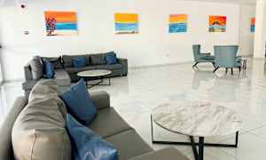 Hotellin aula, jossa on sohvia ja nojatuoleja, seinät koristeltu maalauksilla. (Tekoälyn luoma teksti)