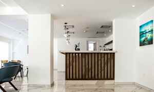 Kuva kirkkaasta ja modernista hotellin vastaanotosta, jossa on marmorilattia, roikkuvia valaisimia ja puinen vastaanottotiski. (Tekoälyn luoma teksti)