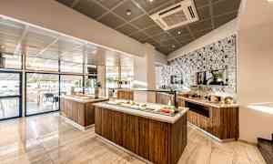 Moderni ja valoisa buffetalue, jossa ruokaa tarjoillaan puutelineillä ja koristeellisella laattojen koristelemalla seinällä. (Tekoälyn luoma teksti)