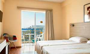 Hotellihuone, jossa on kaksi yhden hengen vuodetta, tuoli, televisio ja parveke, josta on näkymä. (Tekoälyn luoma teksti)