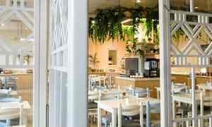 Ravintola, jossa on pöytiä ja tuoleja, sekä koristeltu buffet ja roikkuvia kasveja. (Tekoälyn luoma teksti)