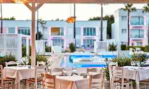 Ravintolapöydät, joissa valkoiset liinat, altaan äärellä, ympäristö modernia arkkitehtuuria. (Tekoälyn luoma teksti)