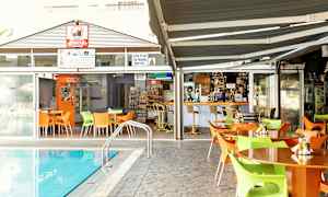 Ulkotila, jossa pöytiä ja tuoleja uima-altaan vieressä, taustalla baari ja ruokailupaikka. (Tekoälyn luoma teksti)