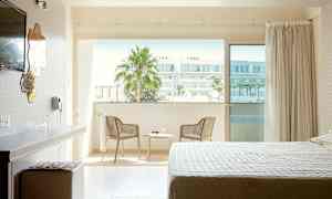 Hotellihuone, jossa on sänky, kirjoituspöytä ja tuoli parvekkeen vieressä, näkymä kaupunkiin. (Tekoälyn luoma teksti)