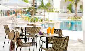 Pöytä korituoleilla uima-allasalueella, jossa on kaksi lasillista mehua ja aurinkohattu tuolilla. (Tekoälyn luoma teksti)