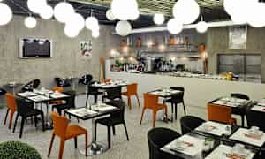 Modernit ravintolakalusteet mustilla ja oransseilla tuoleilla sekä katetut pöydät. (Tekoälyn luoma teksti)