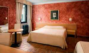 Hotellihuone, jossa on iso sänky, pöytä ja tuolit sekä ikkuna verhoilla. (Tekoälyn luoma teksti)