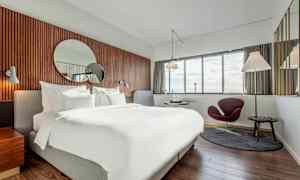 Moderni hotellihuone, jossa suuri sänky, pyöreä peili seinällä ja ikkunat näkymällä. (Tekoälyn luoma teksti)