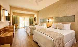 Hotellihuone, jossa on kaksi sänkyä, oleskelutila ja vaaleat kalusteet. (Tekoälyn luoma teksti)