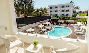 Parveke, jossa kaksi valkoista tuolia ja pöytä, jolla on vihreä kasvi, näkymä uima-altaalle ja aurinkotuoleille. (Tekoälyn luoma teksti)