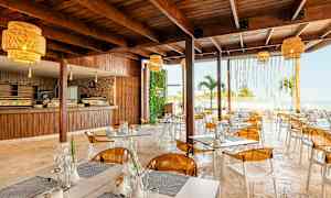 Moderni ravintola, jossa on puukalusteet, keltaiset valaisimet ja näkymä merelle. (Tekoälyn luoma teksti)