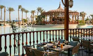 Terassilla katettu pöytä, jolta on näkymä altaalle, jota ympäröivät palmupuut ja paviljonki. (Tekoälyn luoma teksti)