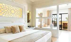 Vaalea ja tyylikäs makuuhuone, jossa hyllyllä koristeellisia maljakoita, suuri sänky tyynyineen ja parvekkeelle kulku. (Tekoälyn luoma teksti)