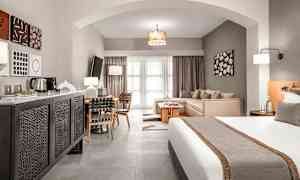 Hotellihuone, jossa on sänky, istuinryhmä ja ruokapöytä, sekä moderni sisustus. (Tekoälyn luoma teksti)