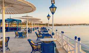 Ulkoravintola, jossa on siniset huonekalut veden äärellä varjojen alla. (Tekoälyn luoma teksti)