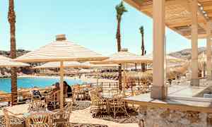 Ulkoilmaravintola bambutuoleilla ja aurinkovarjoilla lähellä rantaa sinisen veden äärellä. (Tekoälyn luoma teksti)