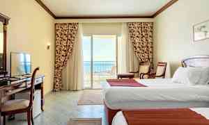 Hotellihuone, jossa on valkoiset seinät, kaksi yhden hengen vuodetta ja parveke merinäköalalla. (Tekoälyn luoma teksti)