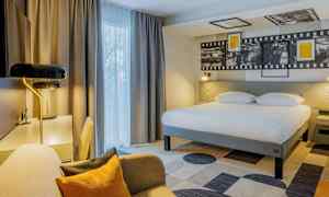 Hotellihuone, jossa suuri sänky, kirjoituspöytä ja istumapaikka. (Tekoälyn luoma teksti)