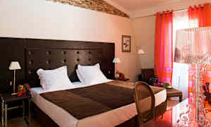 Kuvassa on hotellihuone, jossa on parisänky, tummanruskea sängynpääty ja värikkäät punaiset verhot. (Tekoälyn luoma teksti)