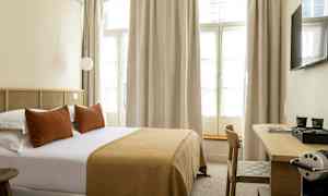 Hotellihuone, jossa on parivuode, tyynyt ja ruskeansävyinen peite sekä työpöytä ja kahvikone. (Tekoälyn luoma teksti)