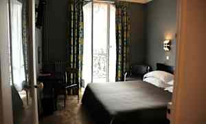 Hotellihuone, jossa on parivuode, pöytä ja tuoli sekä lasiovi, josta on näkymä, ja verhot. (Tekoälyn luoma teksti)