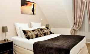 Makuuhuone, jossa on sänky, tyynyt, taideteos seinällä ja verhot. (Tekoälyn luoma teksti)