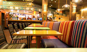 Ravintola, jossa värikkäät pöydät ja tuolit sekä raidalliset penkkipäällysteet. (Tekoälyn luoma teksti)