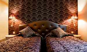 Kaksi vuodetta koristeellisilla päiväpeitteillä ja tyynyillä tumman kuviollisen seinän edessä. (Tekoälyn luoma teksti)