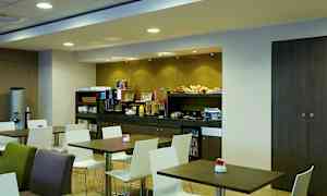 Aamiaishuone, jossa pöytiä ja tuoleja sekä buffetti erilaisine ruoka-aineineen. (Tekoälyn luoma teksti)