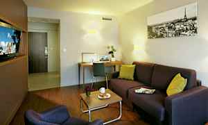 Olohuone, jossa on sohva, nojatuoli, sohvapöytä kahvikupilla ja croissantilla, kirjoituspöytä ja koristeellisia yksityiskohtia. (Tekoälyn luoma teksti)