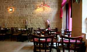 Ravintolatila, jossa on pöytiä ja tuoleja sekä koristekasveja kiviseinän edessä. (Tekoälyn luoma teksti)