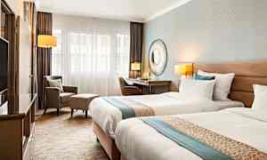 Hotellihuone, jossa kaksi erillistä vuodetta, kirjoituspöytä, tuoli ja nojatuoli. (Tekoälyn luoma teksti)