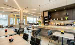 Moderni kahvilaympäristö, jossa istuimia pöytien ääressä ja baaritiskillä, koristeltu kukilla. (Tekoälyn luoma teksti)