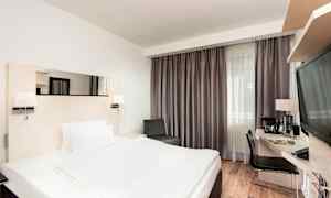 Hotellihuone, jossa on parivuode, kirjoituspöytä ja tuoli sekä suuri ikkuna verhoilla. (Tekoälyn luoma teksti)