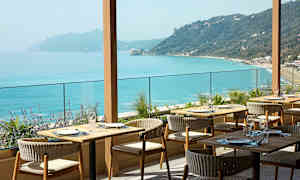 Ravintola ulkoterassilla ja näkymä turkoosille merelle ja kumpuilevalle rannikkoviivalle. (Tekoälyn luoma teksti)