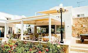 Ulkona sijaitseva ruokailualue, jossa on pöytiä ja tuoleja, rakennuksen läheisyydessä ja kukkien ympäröimänä. (Tekoälyn luoma teksti)