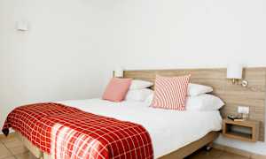 Kahden hengen huone, jossa punaiset vuodevaatteet ja kaksi tyynyä, seinävalaisimet ja yöpöytä. (Tekoälyn luoma teksti)