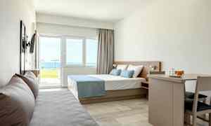 Moderni hotellihuone, jossa sänky, sohva ja ruokapöytä, merinäköala ikkunan ulkopuolella. (Tekoälyn luoma teksti)