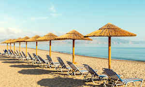 Rivi aurinkotuoleja ja olkipäällysteisiä aurinkovarjoja hiekkarannalla meren äärellä. (Tekoälyn luoma teksti)