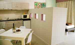 Asunto, jossa on keittiö, joka sisältää työtason, kaapit, mikroaaltouunin ja jääkaapin. Etualalla on valkoinen ruokapöytä tuoleineen. (Tekoälyn luoma teksti)