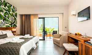 Hotellihuone, jossa on parivuode, istuinryhmä, parveke ja lehtikuvioitu seinäkoriste. (Tekoälyn luoma teksti)