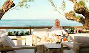 Istuinryhmä meren rannalla, näkymä siniseen veteen ja puihin. (Tekoälyn luoma teksti)