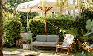 Ulkotila, jossa sohva, lepotuoli ja aurinkovarjo viheralueen ympäröimänä. (Tekoälyn luoma teksti)