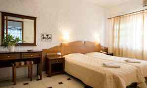 Hotellihuone, jossa on kaksi erillistä vuodetta, puinen lipasto ja valkoiset seinät. (Tekoälyn luoma teksti)